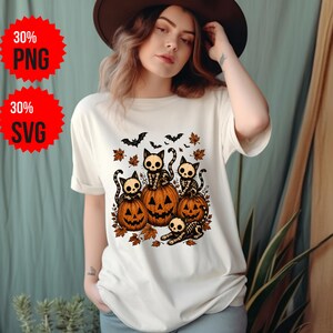 Peut inclure: Un t-shirt à manches courtes de couleur crème avec une impression graphique représentant quatre chats squelettes assis sur et autour de deux citrouilles orange sculptées, entourés de feuilles d'automne et de petites chauves-souris noires.