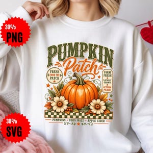 Peut inclure: Un sweat-shirt blanc avec un motif représentant une grosse citrouille orange entourée de fleurs blanches, de blé et de feuilles. Le texte indique PUMPKIN Patch, FRESH FROM THE PATCH, FARM FRESH LOCALLY GROWN AUTUMN PICKED, PUMPKINS, CORN MAZE, APPLE CIDER.