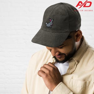K&ouml;nnte beinhalten: Dunkelgr&uuml;ne Cord-Baseballkappe mit einem pixeligen grauen Hasen mit rosa Akzenten. Die Kappe hat einen gebogenen Schirm und eine strukturierte Krone. Das Logo "A/D Atelier Decode" ist sichtbar.