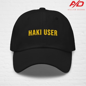 May include: Black baseball cap with the embroidered text "HAKI USER" in gold. The cap has a curved brim and a button on top. The Atelier Decode logo is visible in the upper right corner.