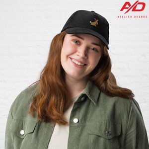 K&ouml;nnte beinhalten: Schwarze Cord-Baseballkappe mit einem gestickten Hund mit Weihnachtsm&uuml;tze. Die Kappe hat einen gebogenen Schirm und eine strukturierte Krone. Das Atelier Decode-Logo befindet sich in der oberen rechten Ecke.