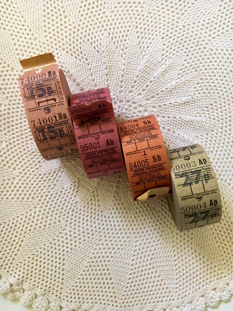 May include: Five vintage bus tickets rolled up and placed on a white crocheted doily. The tickets are from different cities and transportation companies. The tickets are brown, pink, and red.