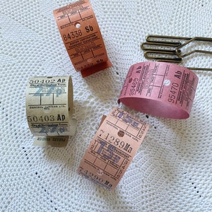 May include: Close-up of four vintage bus tickets from different cities in the United Kingdom. The tickets are in various colors, including pink, brown, and white. The tickets have text that includes the city name, the date, and the fare.