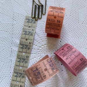 May include: A collection of vintage bus tickets from different cities in the United Kingdom. The tickets are in various colors, including pink, red, and brown. The tickets have the names of the cities and the fares printed on them. There is also a brass hand-shaped paper clip.