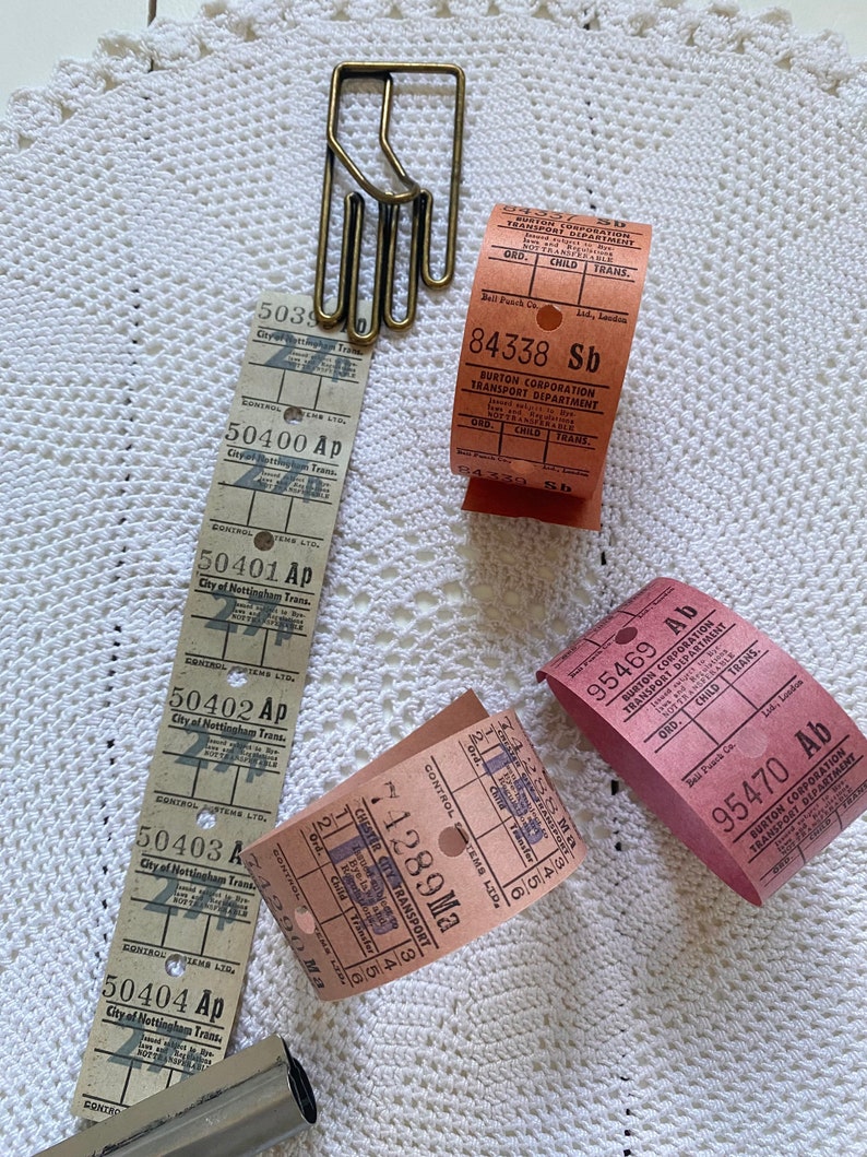 May include: A collection of vintage bus tickets from different cities in the United Kingdom. The tickets are in various colors, including pink, red, and brown. The tickets have the names of the cities and the fares printed on them. There is also a brass hand-shaped paper clip.