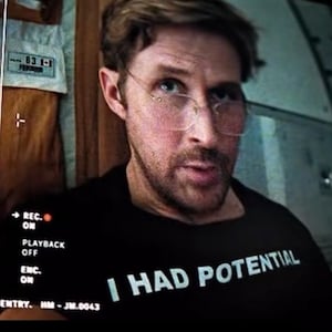 Puede incluir: Un hombre con gafas y una camiseta negra con el texto "I HAD POTENTIAL" en blanco. El hombre está en una habitación con una pantalla que muestra texto y un panel de control. La pantalla dice "LOCATION OBSERVATION ROOM".