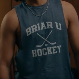 May include: A blue sleeveless shirt with the text "BRIAR U HOCKEY" in white. The shirt features a crossed hockey stick graphic. The person is wearing a silver chain necklace.