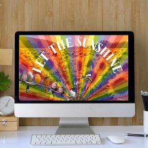 May include: A desktop computer displays a colorful image with the text "LET THE SUNSHINE in". The screen shows birds on a branch against a rainbow background. The desk has a keyboard, mouse, pencils, a mug, and a small plant.