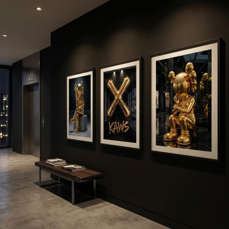 May include: Three framed art prints on a black wall. The prints feature gold sculptures and a gold balloon "X" with "KAWS" text. A bench and elevator are also visible in the hallway.
