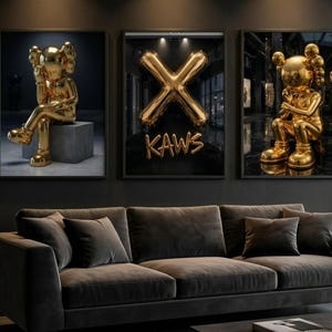 May include: Three framed art prints featuring gold sculptures and a gold balloon "X" with the word "KAWS". The sculptures are in a seated position. The art is displayed above a dark grey sofa.