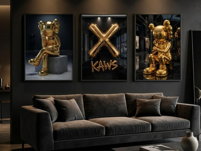 May include: Three framed art prints featuring gold sculptures and a gold balloon "X" with the word "KAWS". The sculptures are in a seated position. The art is displayed above a dark grey sofa.
