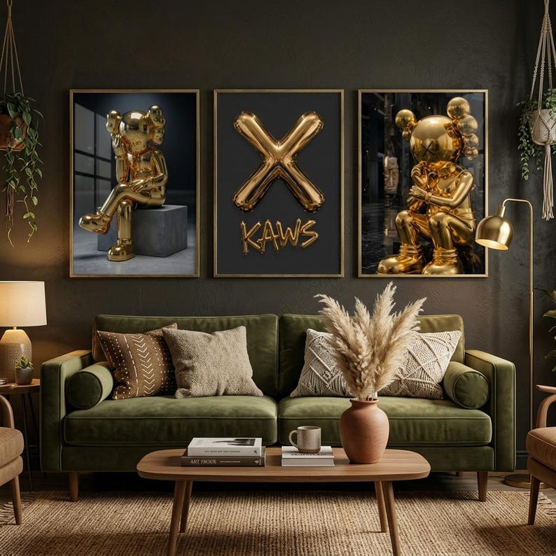 May include: Three framed art prints. The prints feature gold sculptures and a gold 'X' with the word 'KAWS'. They are displayed above a green sofa with decorative cushions. The room has a dark, moody aesthetic.