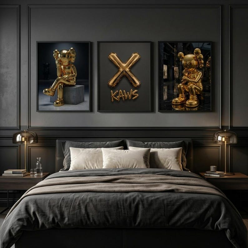 May include: A bedroom scene with three framed artworks. The artworks feature gold sculptures and a gold "X" with the word "KAWS". The bed has a dark grey duvet and pillows. Two gold lamps sit on the bedside tables.