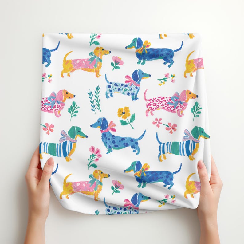 May include: A white fabric featuring a repeating pattern of dachshunds in various colours including blue, yellow, and pink. The dogs are illustrated with bows and wearing patterned clothing like stripes and spots, interspersed with small colourful floral motifs.
