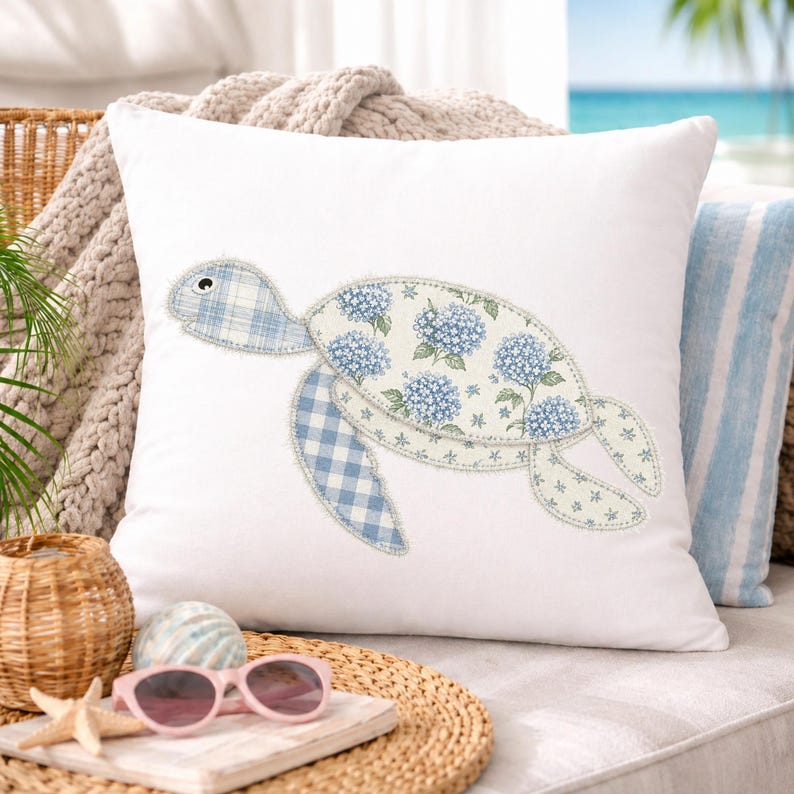 May include: White square pillow featuring a sea turtle design. The turtle's body is decorated with blue hydrangea floral fabric, while the head and flippers have a blue gingham pattern. The pillow is placed on a wicker surface.