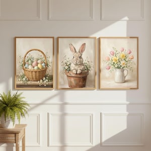 May include: Set of three framed art prints with a spring theme. One print features a basket of pastel-colored Easter eggs, another a bunny in a flower pot, and the third a vase of flowers. The artwork has a soft, vintage aesthetic.