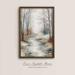 Puede incluir: Una impresión en acuarela enmarcada de una escena de bosque invernal. Árboles desnudos bordean un camino junto a un arroyo, con tonos apagados de gris, marrón y verde. La obra está firmada "Enore Digitale Stories" con el lema "Where Mood Becomes Art."