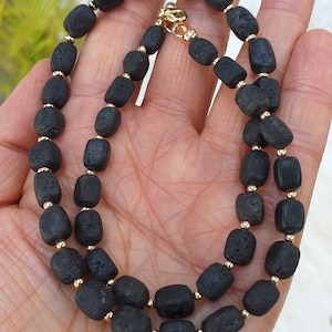 Puede incluir: Un collar de cuentas de lava negra con separadores dorados. El collar mide aproximadamente 45 cm de largo y está hecho de cuentas de lava natural.