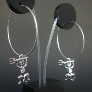 Può includere: Un paio di orecchini a cerchio d'argento con un piccolo ciondolo d'argento di una figura che tiene un tridente appeso a ogni cerchio.