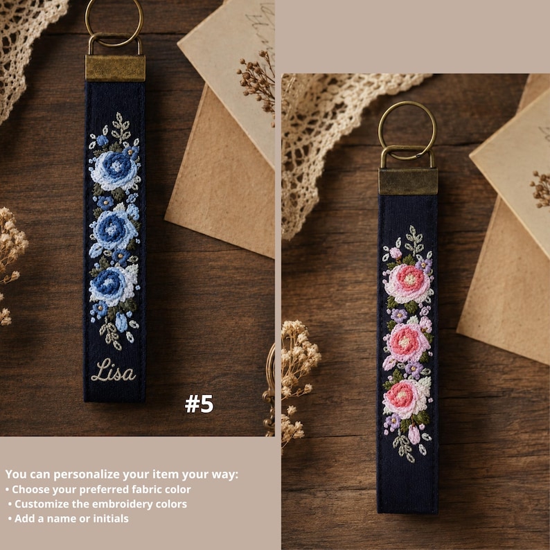May include: Two navy blue fabric keychains with metal rings and bronze-toned hardware. The left keychain features blue floral embroidery and the name Lisa in white script. The right keychain displays pink and purple floral embroidery.