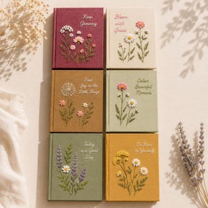 May include: Six rectangular journals with fabric covers in maroon, cream, brown, sage green, olive green, and mustard yellow. Each features embroidered floral designs and text including Keep Growing, Bloom with Grace, Find Joy in the Little Things, Collect Beautiful Moments, Today is a Good Day, and Be Kind to Yourself.