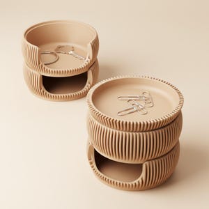 Könnte beinhalten: Zwei beige, gestapelte Schreibtisch-Organizer mit geripptem Design. Ein Organizer enthält Schlüssel und einen Ring, während der andere Büroklammern enthält. Die Organizer haben eine kreisförmige Form mit einem Tablett oben und einem offenen Schlitz unten.