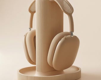 May include: A beige over-ear headphone set resting on a matching beige vertical stand. The stand features a cylindrical, ribbed central column attached to a circular, ribbed base. The headphones have a smooth, solid-colored finish and a mesh headband.