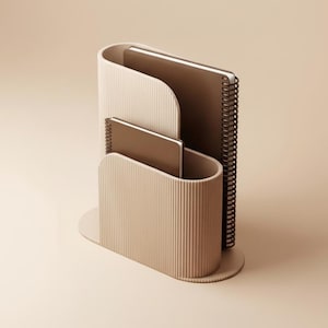 May include: A beige desk organizer with a vertical ribbed texture, featuring two curved compartments of varying heights. Two dark brown spiral-bound notebooks are placed inside the organizer, with one notebook taller than the other.