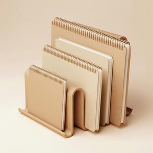 Op de afbeelding: Een set van vier beige spiraalgebonden notitieboeken van verschillende formaten, gerangschikt in een trapsgewijze configuratie. De notitieboeken hebben een minimalistisch ontwerp en een neutraal kleurenpalet, geschikt voor kantoor of persoonlijk gebruik.