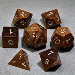 May include: A set of seven polyhedral dice crafted from dark brown wood with engraved numbers filled in silver. The collection includes a d20, d12, d10, d10 percentile, d8, d6, and d4, each displaying clear numerical values across their geometric faces.