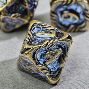 May include: Close-up of several square-shaped beads with a swirling, textured design. The beads feature a metallic gold finish with iridescent blue and purple accents, creating a unique, eye-catching appearance. These beads are ideal for jewelry making.