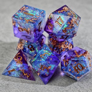 Può includere: Un set di sette dadi poliedrici per giochi da tavolo. I dadi sono di colore viola traslucido con marmorizzazioni interne blu e verdi e numeri e scaglie dorate. Il set include un D4, D6, D8, D10, D12, D20 e un dado percentuale.