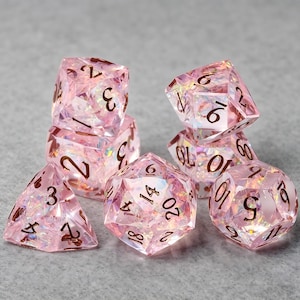May include: A set of seven translucent pink polyhedral dice with iridescent inclusions and dark brown engraved numbers. The collection includes a d20, d12, d10, d8, d6, d4, and a percentile die, all featuring sharp edges and a faceted, gem-like appearance.