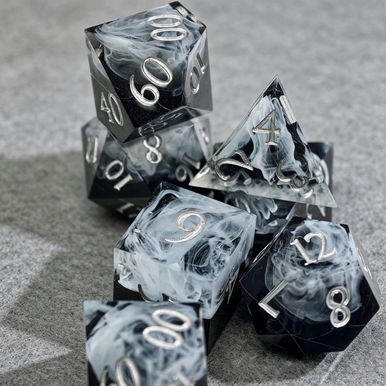 May include: A set of seven polyhedral dice for tabletop games. The dice are black with a swirling white pattern and silver numbering. The dice include a d4, d6, d8, d10, d12, d20, and a percentile die.