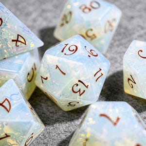 May include: A collection of iridescent, opalescent polyhedral dice. The dice are a pale blue color with brown numbering. The dice are designed for tabletop role-playing games and other dice-based games.