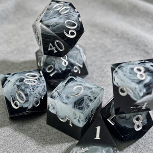 May include: A collection of polyhedral dice in various shapes. The dice are black with a swirling white pattern and silver numbering. The dice are designed for tabletop role-playing games.