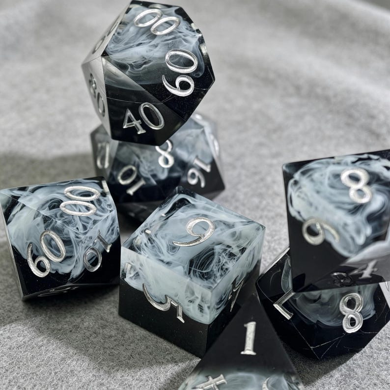 May include: A collection of polyhedral dice in various shapes. The dice are black with a swirling white pattern and silver numbering. The dice are designed for tabletop role-playing games.