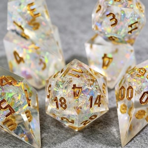 Pode incluir: Conjunto de dados transparentes e iridescentes com números dourados. Os dados são multifacetados, incluindo um dado de vinte lados, e são projetados para jogos de mesa. Os dados têm uma aparência brilhante e brilhante.