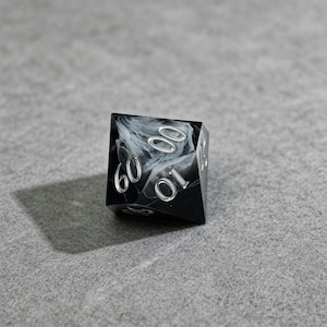 May include: A black and white marbled D6 dice with silver numbering. The dice has the numbers 0, 10, and 60 visible. The dice is sitting on a gray surface.