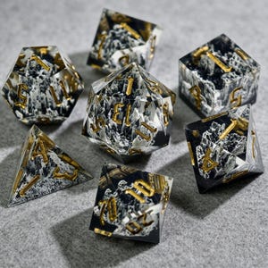 Peut inclure: Ensemble de sept dés polyédriques avec un motif marbré noir et blanc et des chiffres dorés. Les dés sont en résine transparente et sont utilisés pour les jeux de rôle sur table.