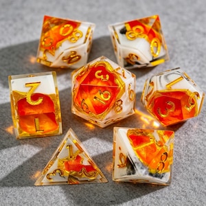 Può includere: Un set di sette dadi poliedrici con un design unico. I dadi presentano una resina trasparente con dettagli arancioni e bianchi, e numerazione dorata. Il set include un D4, D6, D8, D10, D12, D20 e un dado percentuale.