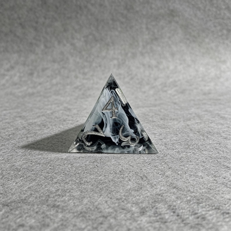 May include: A clear, triangular die with a black and white marbled interior. The number "4" is prominently displayed on the top face, with other numbers visible on the sides. The die is designed for tabletop games.