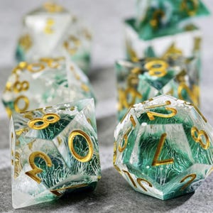 May include: Set of polyhedral dice with a clear, marbled appearance, featuring green and white swirls. The numbers are gold. The dice are designed for tabletop games and role-playing games.