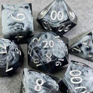 May include: A set of seven polyhedral dice with a black and white marbled design. The dice have silver numbering and are designed for tabletop role-playing games. The dice include a D4, D6, D8, D10, D12, D20, and a percentile die.