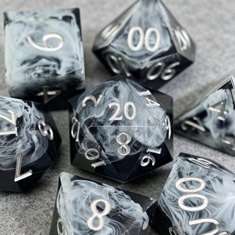 May include: A set of seven polyhedral dice with a black and white marbled design. The dice have silver numbering and are designed for tabletop role-playing games. The dice include a D4, D6, D8, D10, D12, D20, and a percentile die.