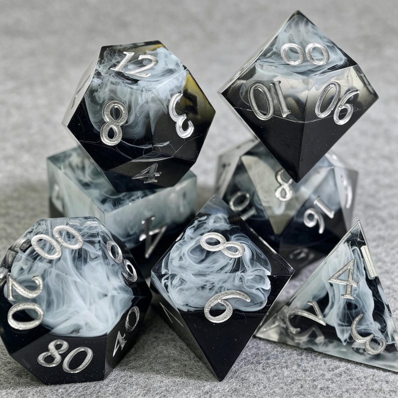 May include: A set of seven polyhedral dice for tabletop games. The dice are black with a swirling white pattern and silver numbering. The set includes a D4, D6, D8, D10, D12, D20, and a percentile die.