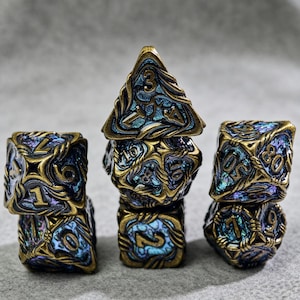 May include: Set of seven polyhedral dice in a fantasy style. The dice are a mix of blue and gold with intricate designs and numbering. The d20 is a pyramid shape, and the other dice are various geometric shapes.