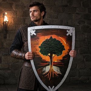 May include: A large wooden heater shield featuring a painted scene of a green tree with visible roots against an orange and black sunset background. The shield has a silver-colored metal border with decorative rivets and corner accents.