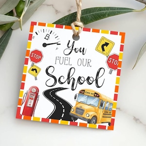 May include: A square tag with the text "You Fuel Our School" features a yellow school bus, a black road, and a red gas pump. The tag has a white background with a border of red, yellow, and orange.