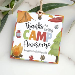 May include: A square gift tag with a camping theme. The tag features a tent, campfire, lantern, canoe, compass, and a pine tree. Text reads "Thanks for making CAMP Awesome. We appreciate all that you do!" The tag is tied with twine.
